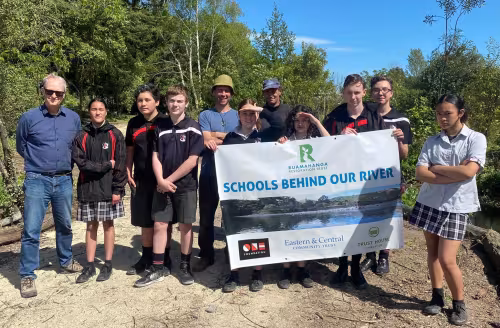 Students holding a "Schools Behind Our River" banner beside the Mākoura Stream