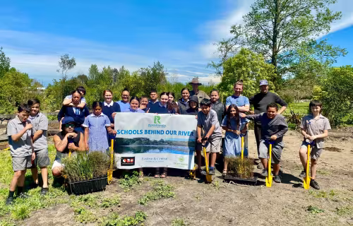 Group of students at a “Schools behind our river” planting day hollding a banner